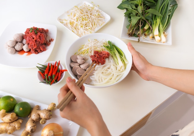 Female chef prepare traditional Vietnamese soup Pho bo with herbs, meat, rice noodles