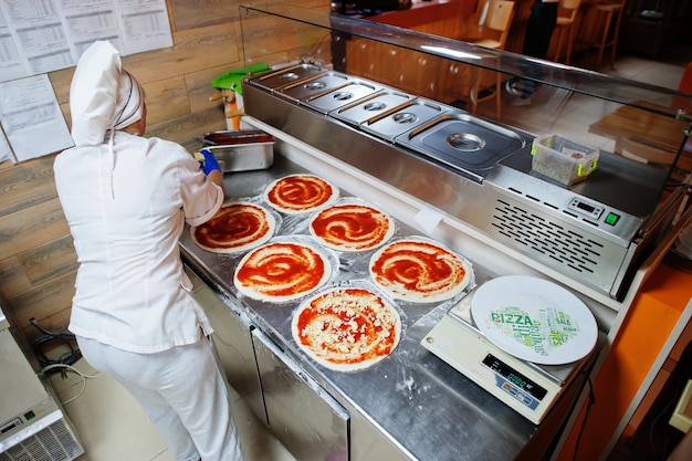 Female chef preparing pizza in restaurant kitchen.