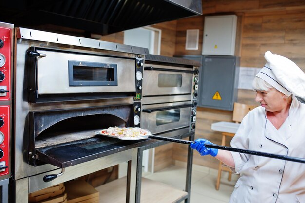 Female chef preparing pizza in restaurant kitchen.