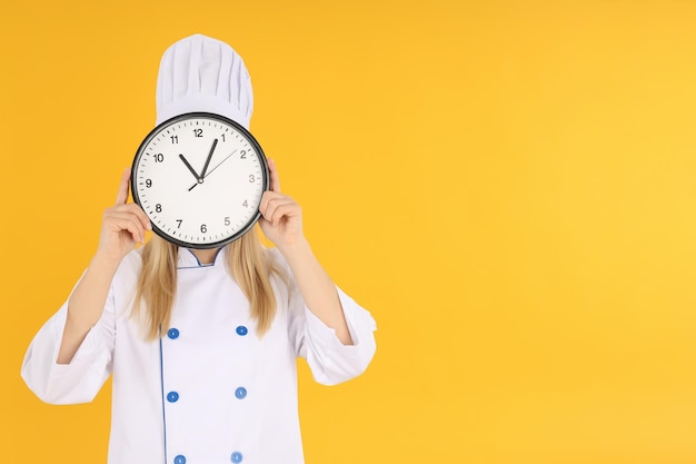 Female chef with clock on yellow background