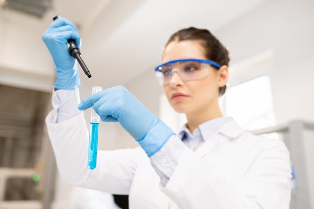 Female chemist dropping reagent into test tube