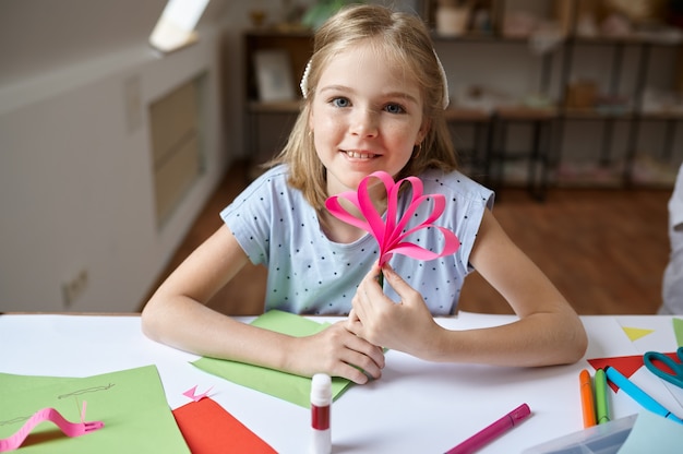 Female child glues colored paper at the table