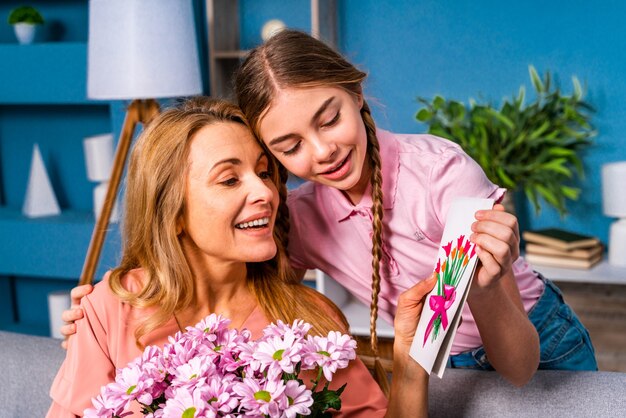 Female child presenting flowers to her mom at home, happy domestic life moments