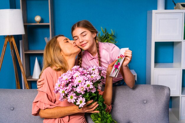 Female child presenting flowers to her mom at home, happy domestic life moments