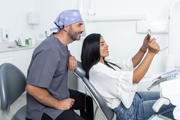 Female client looking at his teeth in the mirror next to a dentist in a room of a dental clinic