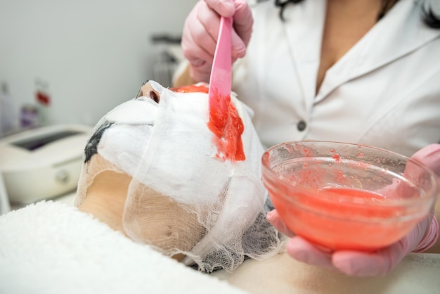 수액 살롱의 여성 고객은 붉은 알지네이트 마스크로 얼굴 노화 방지 치료 절차를 받습니다.