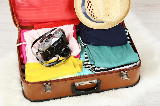 Female clothes and photo camera in old suitcase on light background