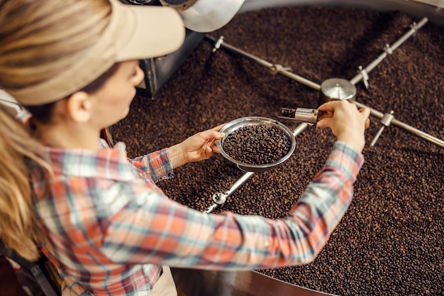 Работница кофейной фабрики контролирует уровень обжарки зерна