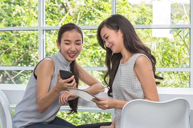 Female colleagues with technologies sitting on chairs at table