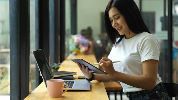 Студентка колледжа делает задание с цифровым планшетом и ноутбуком в кафе