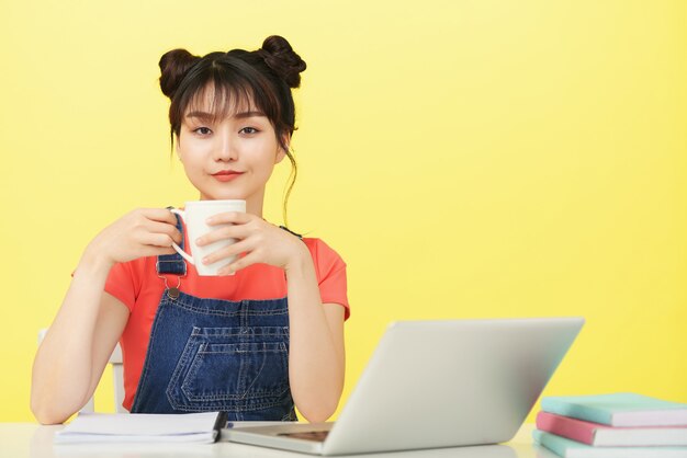 Female college student drinking cup of coffee before having online class