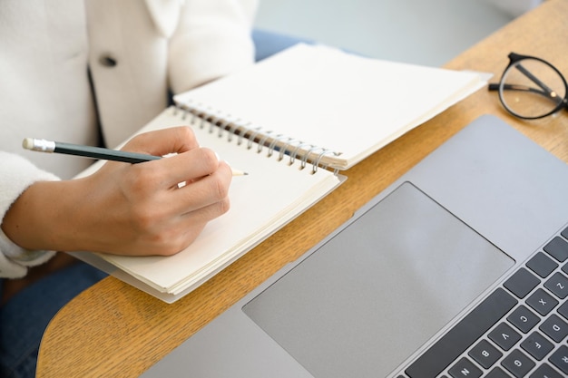 Female college student study on online via laptop and taking lecture on her empty spiral notebook