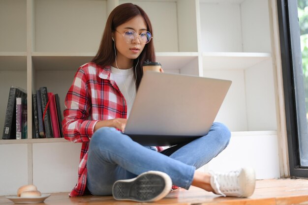 イヤホンをつけてノートパソコンを使ってオンラインクラスで勉強している女子大生