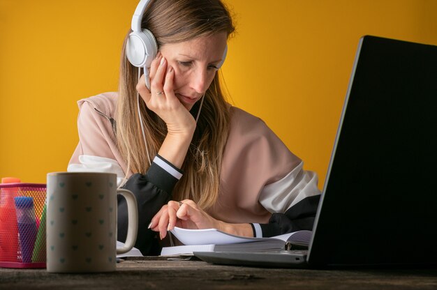 Female college student with headphones listening to a lecture online making notes in her notebook.