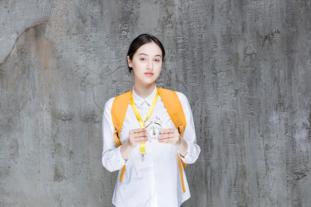 Female college student with yellow backpack holding clock. High quality photo