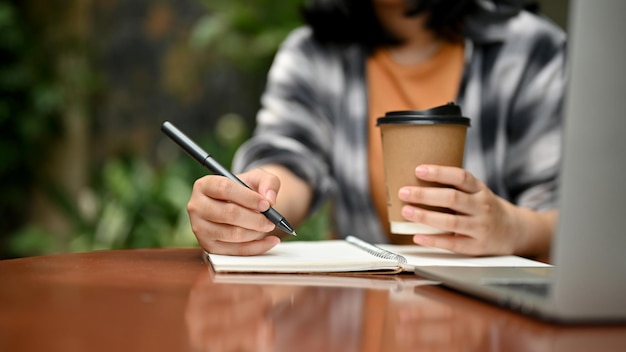 Foto una studentessa universitaria che lavora sui suoi compiti e sorseggia un caffè in un bar all'aperto