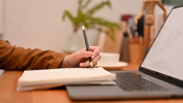 Female college student writing something on her school notebook and using laptop