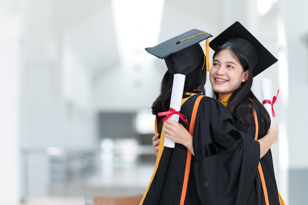 Female college students, university graduates, wearing black hats, yellow tassels, happily embracing friends.