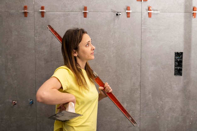 Female construction worker holding a level and trowel checking and admiring well done tiling work on a construction site apartment or house renovation concept