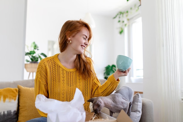 Female consumer unpack parcel receive retail purchase fast postal shipping delivery concept Beautiful young woman is holding cardboard box sitting on sofa at home