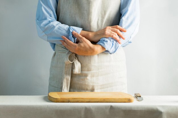 Female cook in cotton apron at the kitchen table with cutting board Rustic natural style Kinfolk concept Copy space