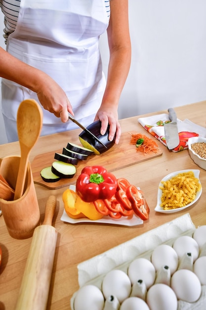 キッチンで木の板にナスを切る女性料理人