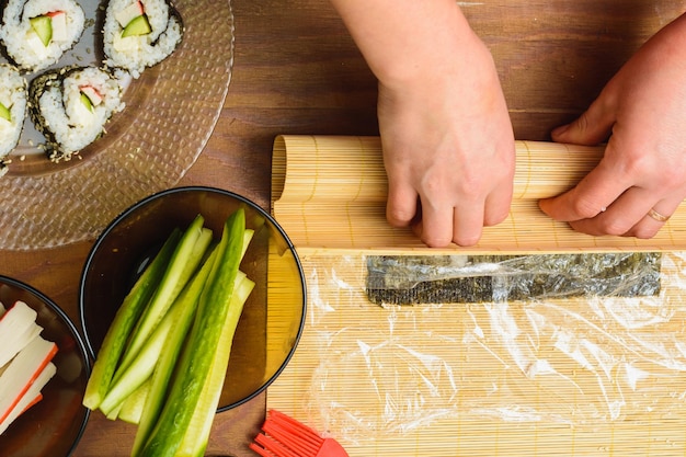 A female cook prepares sushi in the kitchen and wraps a letter to the nori in the roll