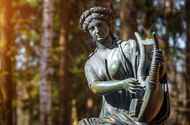 A female copper statue of a deity with a harp in the woods