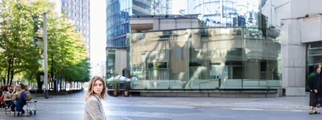 Фото Женщина-работница корпорации, сидящая на открытом воздухе возле офисных зданий, поворачивается назад и оглядывается в ожидании
