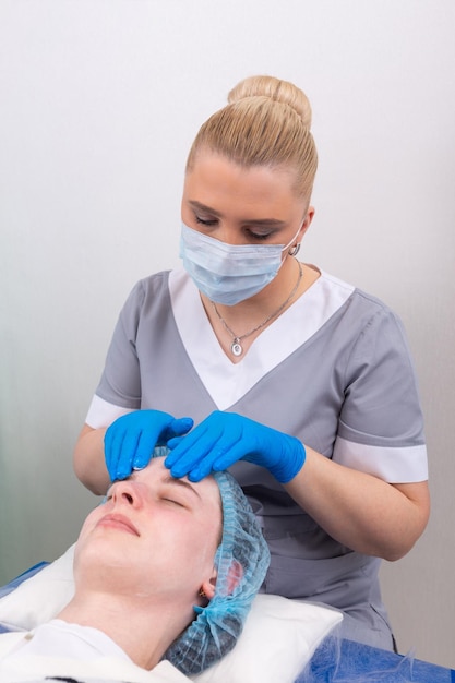 A female cosmetologist manually treats the patient's skin with a moisturizing and toning gel