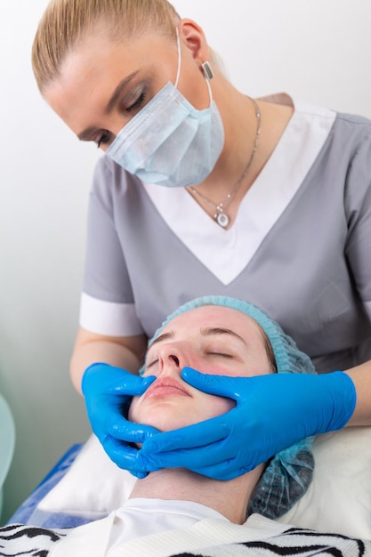 A female cosmetologist manually treats the patient's skin with a moisturizing and toning gel