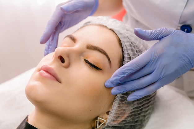 A female cosmetologist manually treats the patient's skin with a moisturizing and toning gel