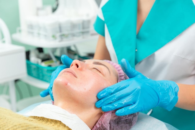A female cosmetologist manually treats the patient's skin with a moisturizing and toning gel