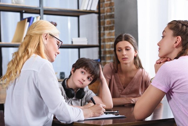 female counselor writing in clipboard on therapy session with family in office