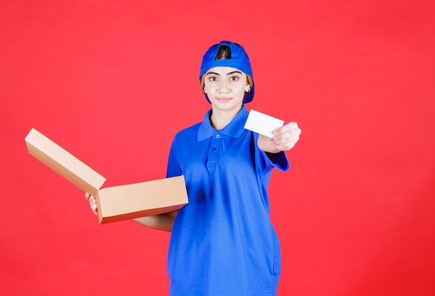 Female courier in blue uniform holding a cardboard takeaway box and presenting her business card. 