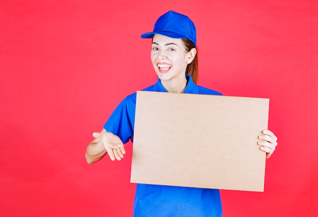 Female courier in blue uniform holding a cardboard takeaway pizza box. 