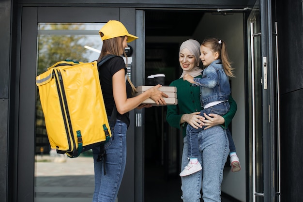 Photo female courier giving pizza boxes and takeaway coffee to smiling happy muslim family