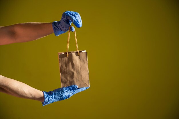 Female courier hand in medical latex gloves holds a small paper bag Safe delivery during the spread of coronavirus Ecofriendly packaging Online shopping