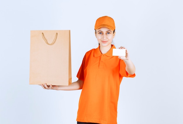 Female courier in orange uniform delivering a shopping bag and presenting her business card