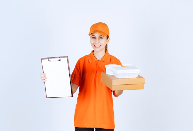 Female courier in orange uniform holding a cardboard box and a plastic takeaway box on it and asking for a signature