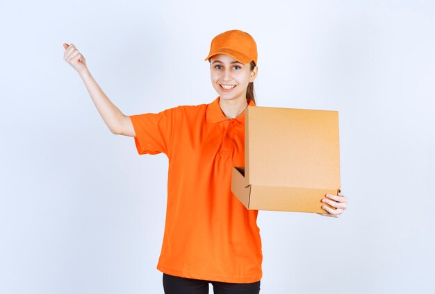 Female courier in orange uniform holding an open cardboard box and showing her fist.