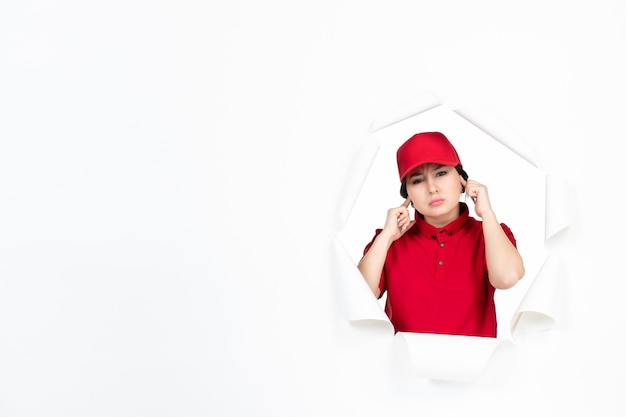 Female courier in red uniform stucking her ears on white