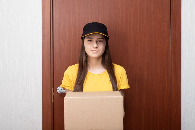 Photo female courier in uniform stands at the door with a box