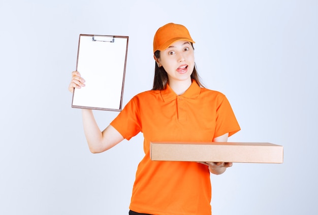 Female courier in yellow uniform holding a cardboard takeaway box and presenting the signature list.