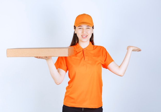 Female courier in yellow uniform holding a cardboard takeaway box .