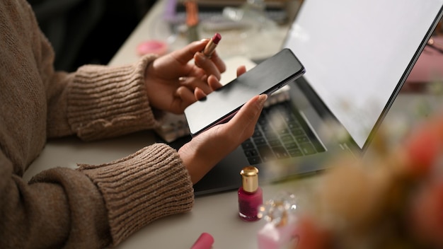 Женщина в уютном свитере использует свой мобильный телефон на своем уютном домашнем рабочем месте, концепция удаленной работы