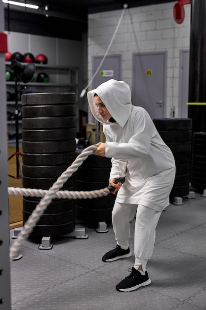 Atleta musulmano crossfit femminile in hijab che lavora fuori con corde pesanti cercando determinante e concentrato di allenamento funzionale atletica fitness attività sportiva rafforzamento della fiducia