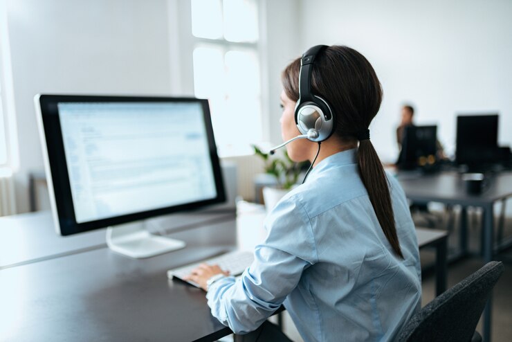 Photo female customer service representative with headset working on computer. rear view.
