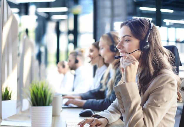 Female customer support operator with headset and smiling with collegues at background