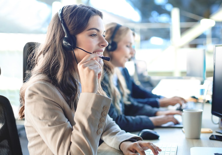 Photo female customer support operator with headset and smiling, with collegues at background.